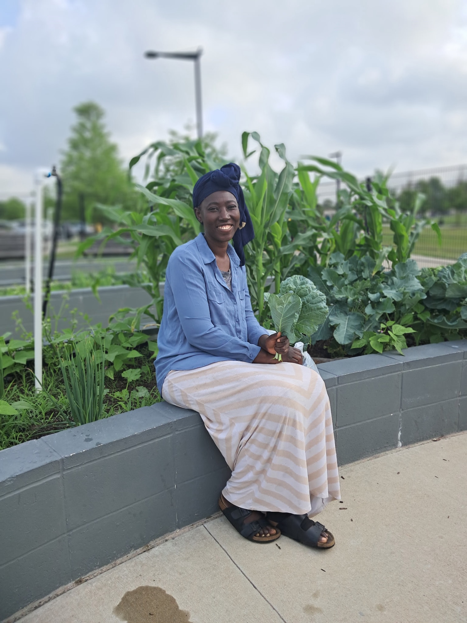 Francisca Hien sitting in the garden holding a collard leaf, with corn and greens behind her